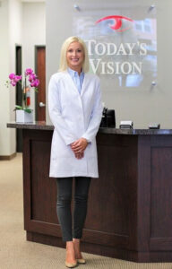 An optometrist stands at the reception desk of her practice as she discusses the benefits of Eyefinity Practice Management and Electronic Health Records.